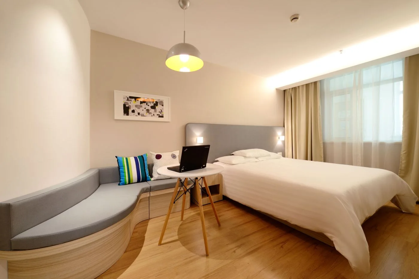 Bedroom with a white bed, curved grey sofa and a small round table